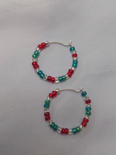 A pair of red, silver lined and green glass seed bead earrings, with a silver 'stopper bead' at the end to stop them easily slipping off the silver hoop.  The hoop has a diameter of approx. 2.3cm. these are quite delicate hoops so care must be taken when putting in and taking out. A fun, festive pair of unique, handmade earrings, with a Christmassy style, ideal for the festive time of year. I can also make in alternative colour combinations if needed, just send me a message with your requirements! To keep your jewellery in the best condition for the longest period, please note:  - Remove jewellery before bathing, showering or swimming.  - Avoid direct contact with body lotions, perfumes and any other chemicals. - Remove jewellery before sleeping. - When not in use, store jewellery in it's Festive Nickel-free Hoop Earrings, Festive Nickel-free Dangle Hoop Earrings, Nickel-free Hoop Earrings For Festive Occasions, Nickel-free Hoop Earrings For Festivals, Festive Red Hoop Jewelry, Red Hoop Jewelry For Festive Occasions, Red Sterling Silver Hoop Earrings, Red Sterling Silver Round Hoop Earrings, Handmade Round Christmas Earrings