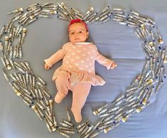 a baby laying on top of a heart made out of silver tubes with a red bow in it's hair