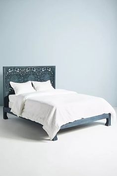 a bed with white sheets and pillows in a room that is painted light blue, has an intricate headboard