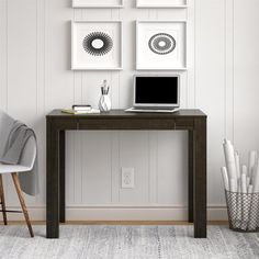 a laptop computer sitting on top of a wooden desk next to a white chair and wall