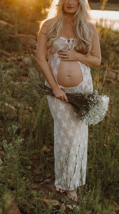 a pregnant woman standing in the grass with her hands on her belly and holding flowers