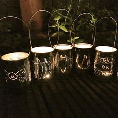 six tin can lights with the word love written on them and some plants in the background