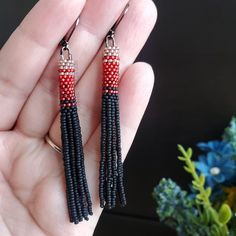 a pair of red and black seed beaded earrings on a person's hand