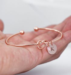 a hand holding a gold bracelet with a initial charm