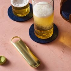 two glasses of beer and a bottle opener on a pink table with blue placemats