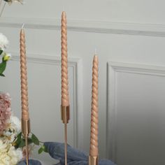 three candles sitting on top of a table with flowers in the backgroung