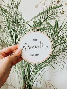 someone is holding up a personalized embroidery ornament in front of a potted plant