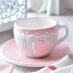 a pink cup and saucer sitting on top of a white place mat next to a window