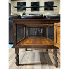 a wooden table with a glass top and legs in front of a black leather couch