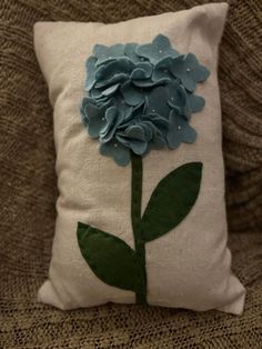 a blue flower is on the back of a white pillow with green leaves and dots