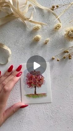 a woman's hand with red nail polish holding up a card that has a tree on it