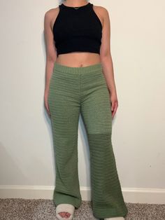 a woman standing in front of a white wall wearing green pants and black crop top