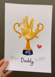 a hand holding up a card with the words best daddy ever written on it and an image of a golden trophy