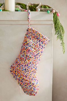 a colorful christmas stocking hanging from a white wall next to a candle and wreath