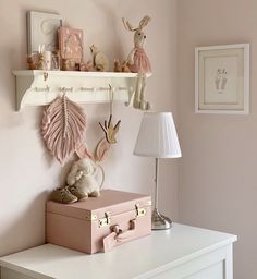 a white dresser topped with a pink suitcase next to a shelf filled with stuffed animals