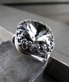 "Exquisite, timeless, classic. This romantic crystal ring features a sophisticated 'Black Diamond' Swarovski crystal in a perfectly-faceted cushion-cut style. The sparkling charcoal grey crystal is enveloped in a highly-detailed, vintage-inspired antiqued silver plated bezel. The antiqued silver-plated ring comfortably adjusts to fit approx. sizes 6 to 10. - Cushion-cut Swarovski crystals: 1/2\" square (12mm) - Antiqued silver plated adjustable ring: fits approx. sizes 6 to 10 Coordinating Shy S Elegant Faceted Crystal Ring For Wedding, Elegant Faceted Crystal Wedding Ring, Formal Silver Faceted Crystal Ring, Silver Faceted Crystal Ring For Formal Occasions, Elegant Square Cut Crystal Ring For Formal Events, Elegant Crystal Rings For Evening, Silver Wedding Ring With Cushion Cut, Elegant Evening Crystal Rings, Classic Crystal Ring