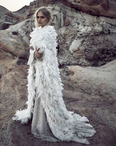 a woman standing in the desert wearing a white feathered coat and silver dress with her hands on her hips