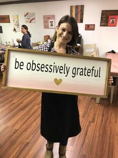 a woman holding up a sign that says be obsesively grateful in front of her