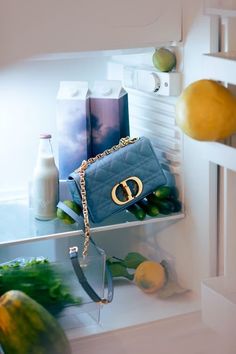 a blue purse sitting on top of a refrigerator freezer next to lemons and cucumbers