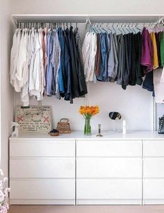 a white dresser topped with lots of clothes next to a vase filled with flowers and a handbag