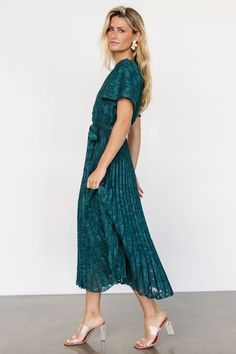 Step into sophistication with the Mindy Pleated Dress in deep emerald green. Faux applique florals, bloused bodice, flutter sleeves, and ankle-length pleated skirt ensure timeless elegance, with a natural waist, detachable sash, and full lining for comfort. Deep Emerald Green, Modest Style, Baltic Born, Ankle Length Skirt, Chiffon Material, Cup Size, Pleated Dress, Flutter Sleeve, Scoop Neckline