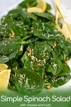 spinach salad with cheese and nuts on a white plate next to lemon wedges