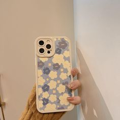 a person holding up a phone case with flowers on it in front of a wall