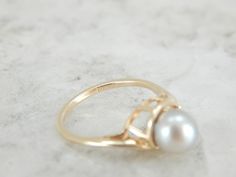 Simple and classic, this pearl ring has a well proportioned gold band, and four balanced prongs set on each side of the pearl. The pearl has a creamy grey luster with pink undertones and makes the perfect understated piece. Metal: 14K Yellow Gold Gem: Grey Pearl Gem Measurements: 6.4 mm, Round Accents: Diamond .04 Carat Ring Size: 4.25 Marks: "14K" Stamped on the inside band Classic Oval Akoya Pearl Ring, Pearl Grey, The Pearl, Gold Band, Pearl Ring, Cocktail Ring, Diamond Solitaire, Cocktail Rings, Gold Bands