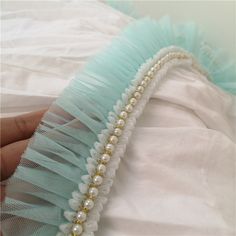 a hand holding a white and blue garter with pearls on it