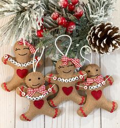 three gingerbread christmas ornaments hanging from a pine cone on a white wooden table with evergreen branches