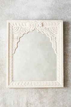 an ornate white mirror on the wall with a light colored background and textured paper