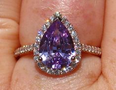 a woman's hand holding an engagement ring with a large purple stone in the center