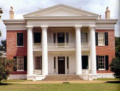 a large white house with columns and pillars on the front lawn, surrounded by trees