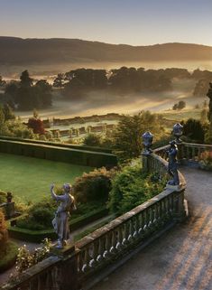 an aerial view of a garden with statues in the foreground and misty hills in the background