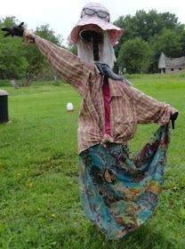 a woman in a dress and hat standing on the grass with her arms spread out