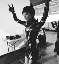 a woman dressed in latex and holding her hands up to the side while standing on a hard wood floor