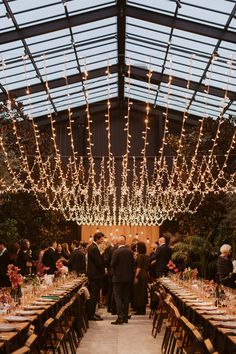 a group of people standing around tables with lights hanging from the ceiling