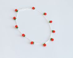 a white string with red beads and green leaves on it is attached to a beaded necklace