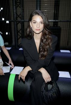 a woman sitting on top of a black bench holding a purse and looking at the camera