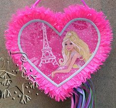 a pink heart shaped pinata with the eiffel tower in the background and some tassels hanging from it