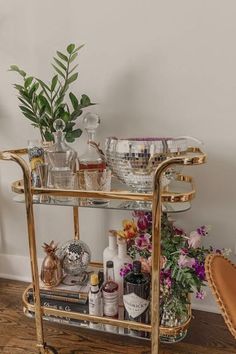 a gold bar cart filled with bottles and glasses on top of a hard wood floor