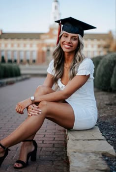 a woman in a graduation cap and gown sitting on a brick wall with her legs crossed