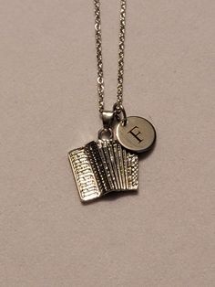 a silver necklace with an initial on it and a small accordion charm hanging from the front