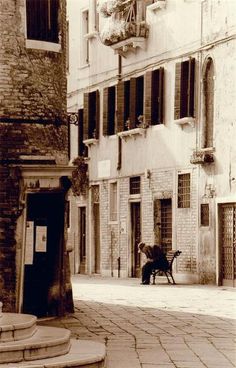 a black and white photo of a person sitting on a bench in an alleyway