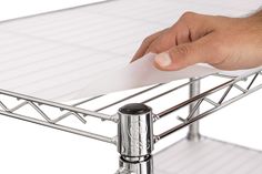 a hand holding a piece of paper on top of a metal shelf with two legs