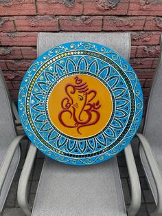 a blue and yellow plate sitting on top of two gray chairs next to a brick wall