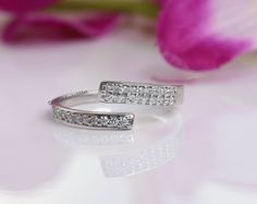 two white gold wedding rings with diamonds on them and a pink flower in the background