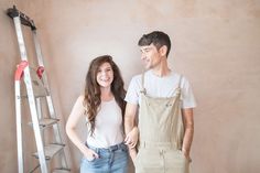 a man and woman standing next to each other in front of a wall with ladders