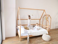 two children are sitting on a bed in a room with wood floors and white walls