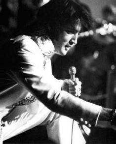 black and white photograph of a man holding a microphone in his right hand while sitting down